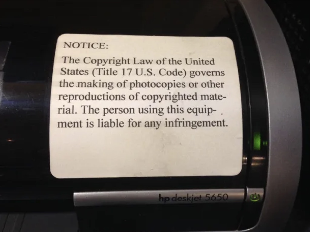 Photograph of a copy machine with a label on the side warning peopel to not break the rules />
            </div>
            <div class=