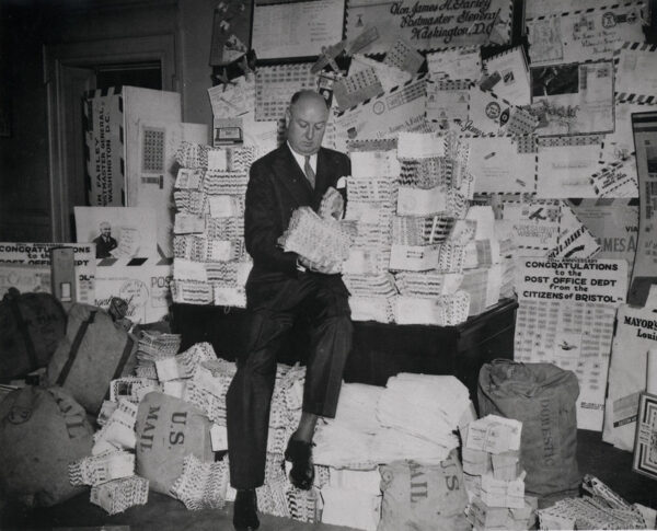 a man sititng in front of a desk which is piled high with neatly organized mail